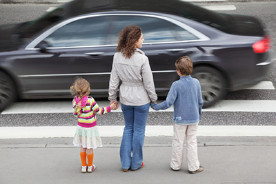 A woman and two children wait to cross a busy road