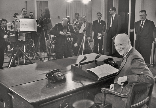 Eisenhower smiles at a desk with a microphone